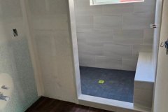 Newly installed bathroom shower featuring stylish tiled walls and dark wooden flooring for a contemporary look.