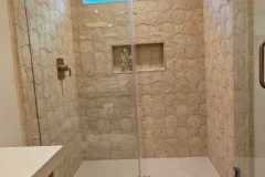 Elegant bathroom with stone tiles, glass shower, and wooden accents.
