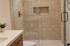 Elegant bathroom featuring a spacious shower with beige stone tiles and a glass enclosure, showcasing quality tile work.