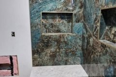 Luxurious bathroom with blue and brown marble tiles, featuring a built-in shelf and a bench.