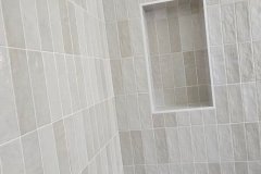 This image shows a modern shower wall with beige tiles and a recessed niche for toiletries, highlighting quality tile work by Grapme Tile Works Corp.