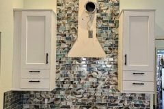 Stylish kitchen featuring a mosaic tile backsplash from Grapme Tile Works, complemented by white cabinetry and wooden accents.
