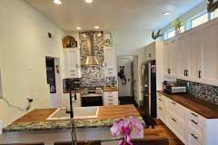 A spacious kitchen featuring white cabinetry, a mosaic tile backsplash, and wooden countertops, showcasing contemporary design and functionality.