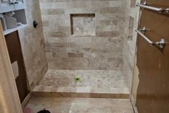 Elegant bathroom featuring beige stone tiles and a built-in niche for toiletries.