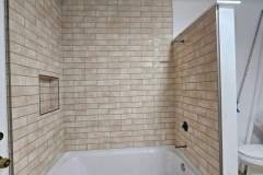 Contemporary bathroom featuring beige brick tiles, a white bathtub, and a separate toilet area.