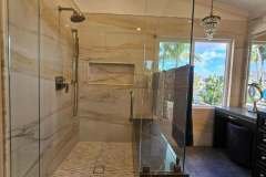 Elegant bathroom featuring a spacious glass shower with marble tiles and a large window overlooking a lush outdoor scene.