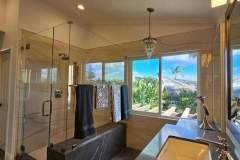Spacious bathroom featuring a glass shower, a large window with a view of lush greenery, and contemporary fixtures.