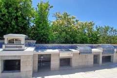 This outdoor kitchen features stone countertops, built-in grills, and ample space for cooking and social gatherings.