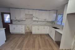 Spacious kitchen featuring white cabinetry, marble backsplash, and wood flooring, ideal for modern home interiors.